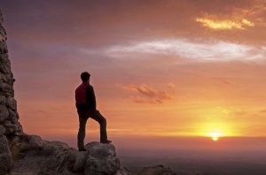 Man on top of a mountain standing contemplates the dawn